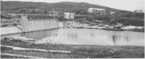  Oppdemminga av Essandsjøen begynte i 1940, og i 1943 starta TEV arbeidet med å bygge en varig og større dam. Bildet er fra 4. oktober 1943, og her er arbeidsbrakka kommet på plass. Vi ser dessuten båten som ble brukt til frakting av folk og materialer over sjøen fram til damstedet.